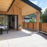 Moderne Holzterrasse mit Tisch und St&uuml;hlen, umgeben von B&auml;umen und Geb&auml;uden im Hintergrund.