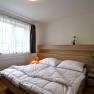 Modern bedroom with double bed, light wooden furniture and large windows with white curtains.