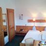 Ein Hotelzimmer mit zwei Einzelbetten, Holzm&ouml;beln und gr&uuml;ner Teppichboden.