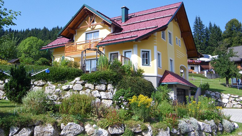 Yellow house with a red roof in a green landscape.