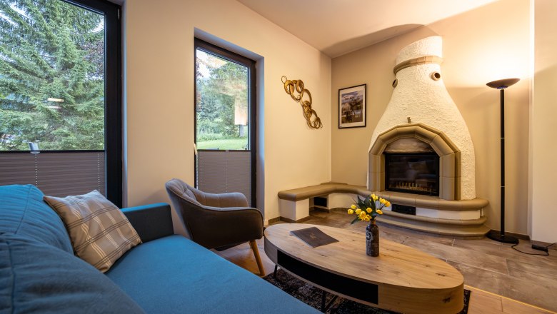 Cozy living room with fireplace, sofa, armchair and coffee table. Large windows with a view of the greenery.