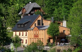 Ein traditionelles Geb&auml;ude mit Holzfassade in einer gr&uuml;nen Waldlandschaft.