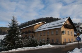 A yellow building in the snow with the inscription 'Pension zur Post'.