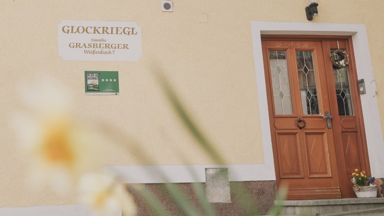 Eingangst&uuml;r eines Geb&auml;udes mit dem Schild 'Glockriegl' und einem Blumenkranz.