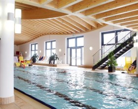 Innenansicht eines Schwimmbads mit Holzdecke und großen Fenstern.