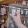 A hand reaches for a jar of homemade redcurrant jam on a shelf.