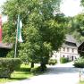 A traditional farmhouse with a garden and flags in the foreground.