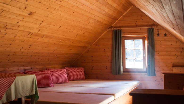 Gemütliches Dachzimmer mit Holzverkleidung, Betten und karierten Kissen.