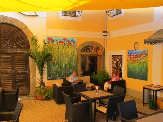 A cozy inner courtyard of a caf&eacute; with yellow walls, plants and paintings. Two people are sitting at a table.