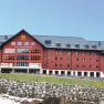 Großes rotes Gebäude des Jufa Sport Resorts in einer bergigen Landschaft.