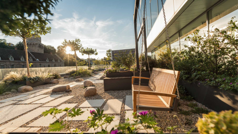 Garden with rocking bench, gravel path and plants, in the background a castle at sunset.