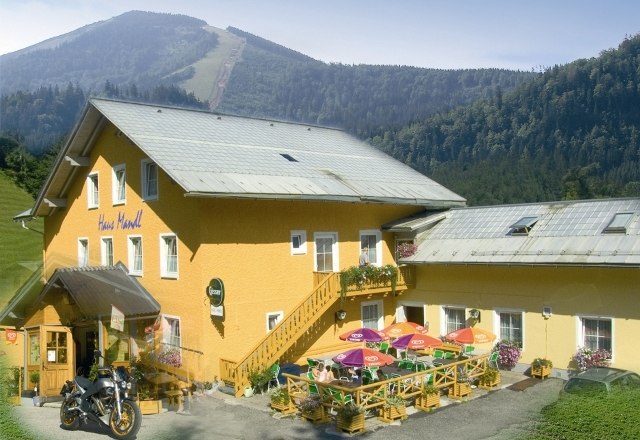 Gelbes Gebäude mit Terrasse und bunten Sonnenschirmen, umgeben von Bergen.