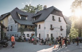 Ein traditionelles Gasthaus mit Menschen im Freien bei Sonnenschein.