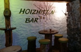 Rustic bar with wooden furniture and 'Hoizhitt'n Bar' lettering on the wall.