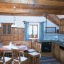 Rustikale K&uuml;che mit Holzm&ouml;beln, Esstisch und St&uuml;hlen, Herd, Sp&uuml;le und Fenster mit karierten Vorh&auml;ngen.