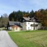 Ein großes, zweistöckiges Haus mit Balkon, umgeben von Wiesen und Bäumen im Herbst.
