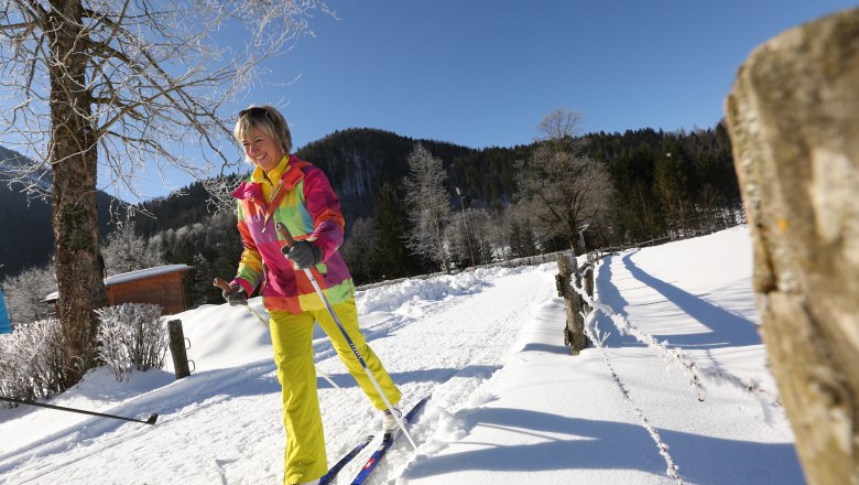 A woman cross-country skiing on a snow-covered trail with a blue sky in the background.