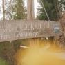 Holzschild mit der Aufschrift 'Familienbauernhof Glockriegl Fam. Grasberger' an einem Waldweg.