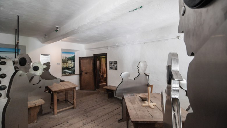 Interior with wooden floor and metal figures at wooden tables.