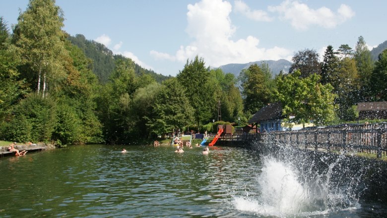 Menschen schwimmen und spielen im Seebachbad Lunz am See, umgeben von Bäumen und Bergen.