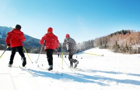 Three people cross-country skiing on a snow-covered trail under a blue sky.