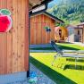 Wooden cabins decorated with fruit and deck chairs on a meadow, surrounded by mountains.