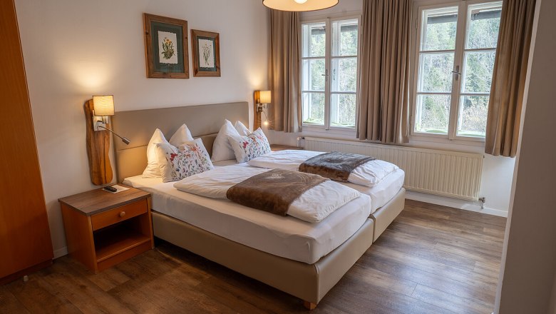 Ein gem&uuml;tliches Schlafzimmer mit zwei Einzelbetten, Holzboden und gro&szlig;en Fenstern mit Blick auf die Natur.