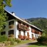 Ein traditionelles Haus mit Blumenkästen vor einem bewaldeten Berg.