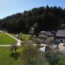 L&auml;ndliche Szene mit einem gelben Haus und Scheunen, umgeben von gr&uuml;nen Wiesen und W&auml;ldern.