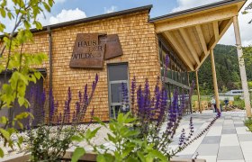 Geb&auml;ude mit Holzfassade und Schild 'Haus der Wildnis', umgeben von Pflanzen.