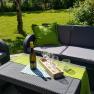 Gartenmöbel mit Weinflasche und Gläsern auf einem Tisch im Freien.