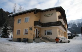 A yellow building with the inscription 'Gasthof Sonnenhof' in the snow, surrounded by mountains.