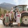 Eine Familie in traditioneller Tracht steht vor einem Traktor in einer l&auml;ndlichen Berglandschaft.