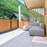 Moderne Terrasse mit Holzw&auml;nden, grauem Sofa und Blick auf bewaldete H&uuml;gel.