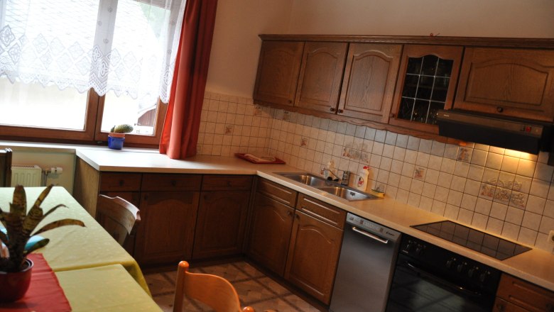Fox farm, © Fuchsbauernhof Kitchen with wooden cupboards, sink, stove and dishwasher. Window with curtain and potted plant on the table.