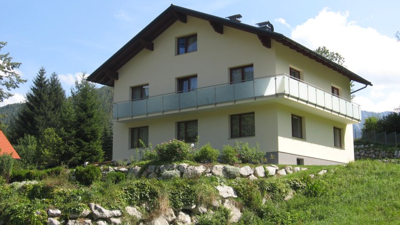 Family Hötzel, © Familie Hötzel A two-storey house with balcony in a green, hilly landscape.
