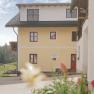 Gelbes Haus mit Holzbalkon und Blumen im Vordergrund.