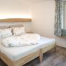 Ein gem&uuml;tliches Schlafzimmer mit einem Holzbett, dekoriert mit Pflanzenmotiven auf Bettw&auml;sche und Vorh&auml;ngen. Ein Fenster mit Sitzbank bietet Ausblick nach drau&szlig;en.