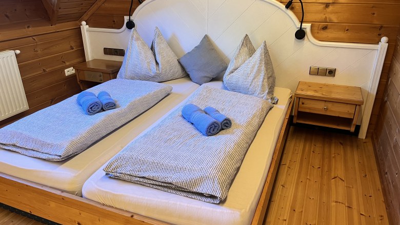 A cozy bedroom with wooden walls and a double bed decorated with blue towels and striped bedding.