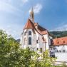 Historisches Geb&auml;ude mit rotem Dach und Turm, umgeben von B&auml;umen.