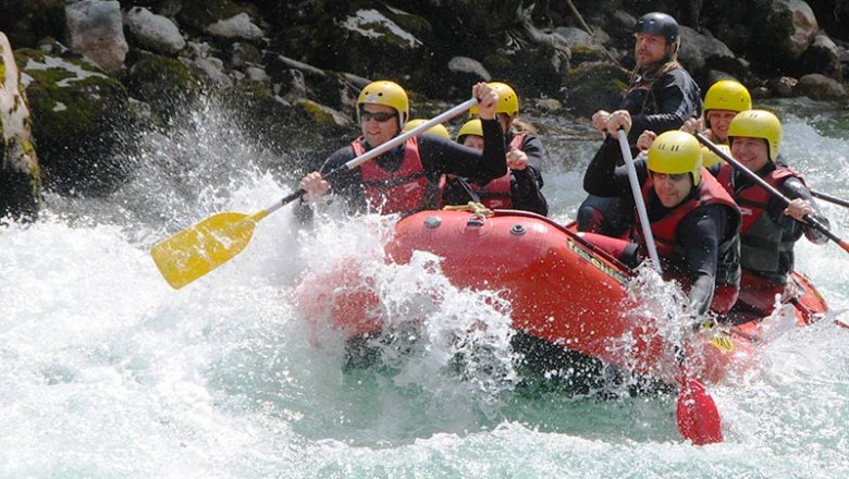 Group rafting on a river with yellow helmets and red vests.