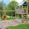 Kinder spielen auf einem Spielplatz mit Schaukel, Rutsche und Kletterturm in einer gr&uuml;nen Umgebung.