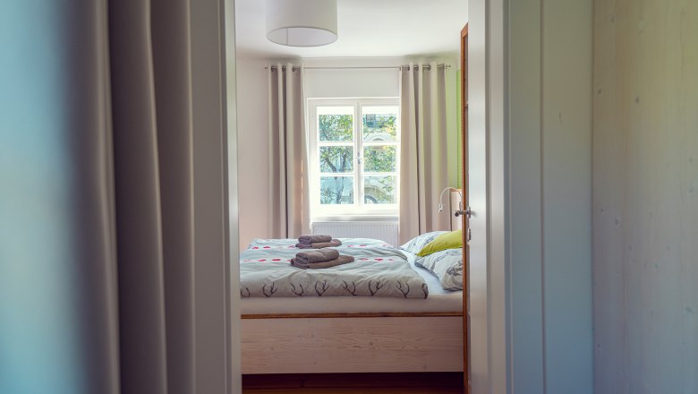 A cozy guest room with a double bed, bed linen with deer motifs and folded towels on the bed, seen through an open door.
