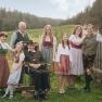 Eine Familie in traditioneller Tracht posiert im Freien vor einer l&auml;ndlichen Kulisse mit Wiesen und B&auml;umen.