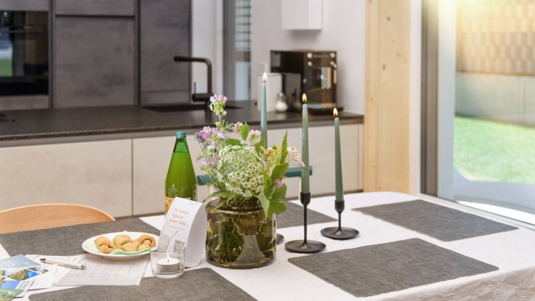 Ein gedeckter Tisch in einer modernen K&uuml;che mit Blumen, Kerzen und Snacks.