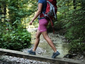 Woman in hiking outfit balancing on wooden posts over a small stream.