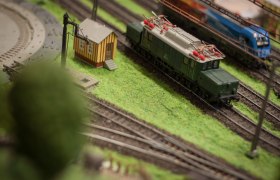 Modelleisenbahn mit grünem Zug und kleinem Gebäude auf einer Anlage.
