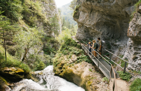 A picturesque hiking trail meanders along the rushing water, surrounded by lush greenery and majestic rocks. Families enjoy the fresh air and breathtaking views of nature as they discover the beauty of the &Ouml;tscher Torm&auml;uer Nature Park.