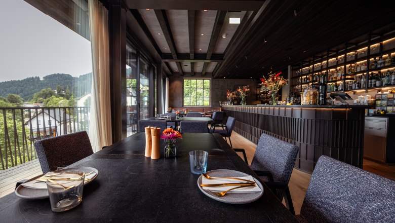 Innenansicht eines modernen Restaurants mit gedecktem Tisch und Bar im Hintergrund.