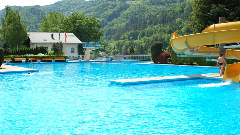Ein Freibad mit Rutsche, Sprungbrett und umliegenden Bergen.